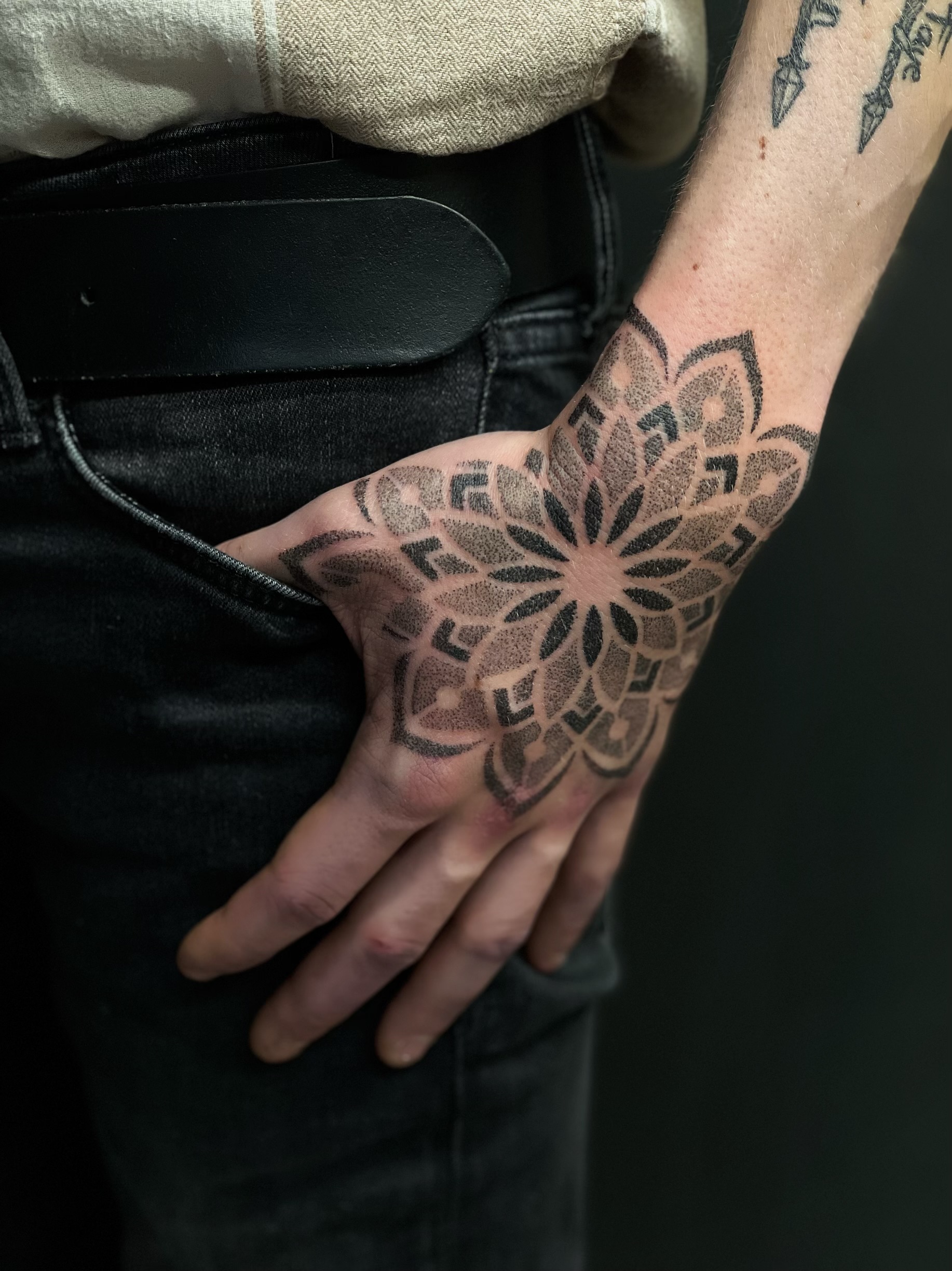 Grote dotwork mandala tattoo op de bovenkant van een hand.