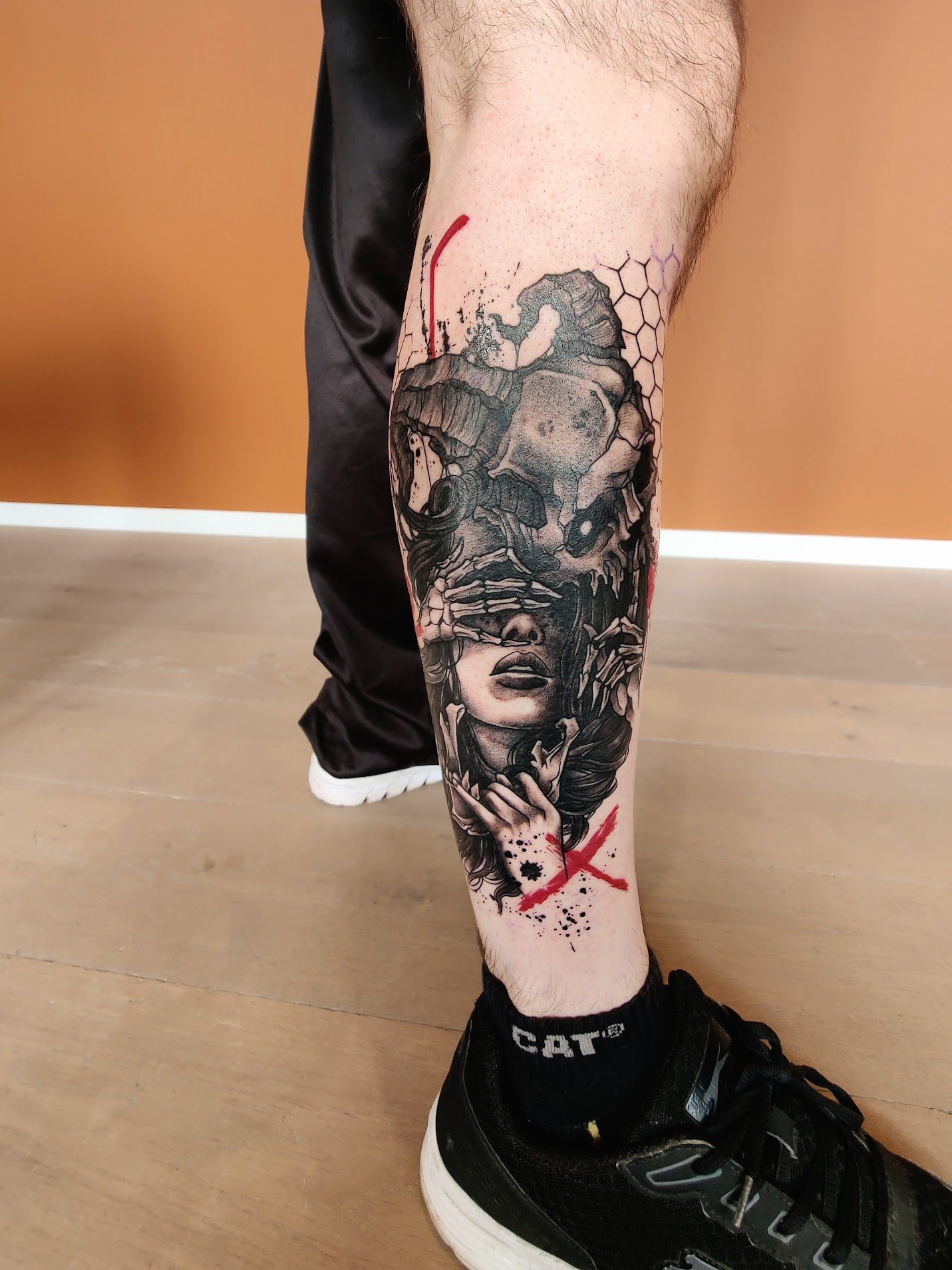 Trash Polka tattoo van een vrouw met een ramschedel en rode accenten op het onderbeen.