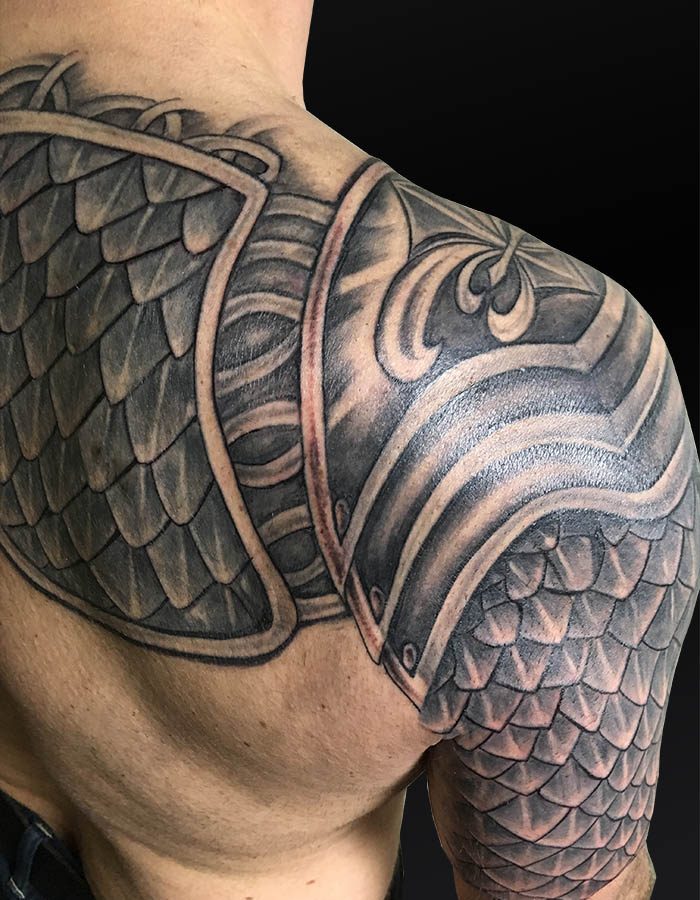 Realistische zwart-wit tattoo van een schubbenharnas op schouder en bovenarm.