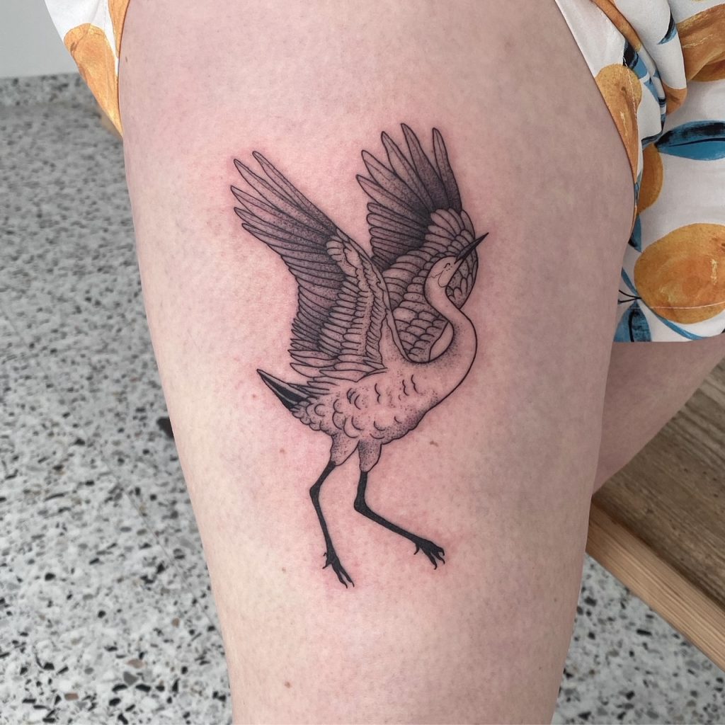 Zwart-wit dotwork tattoo van een reiger met gespreide vleugels op het bovenbeen.