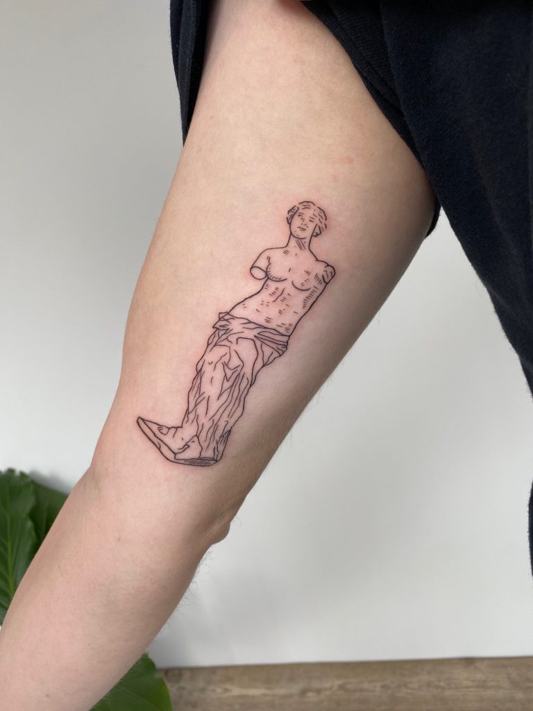 Fineline tattoo van de Venus van Milo standbeeld op bovenarm.
