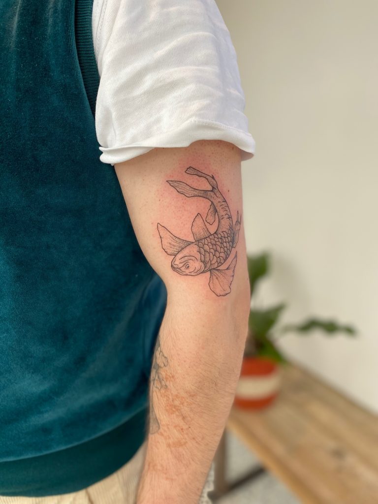 Fineline koi vis tattoo op de bovenarm.