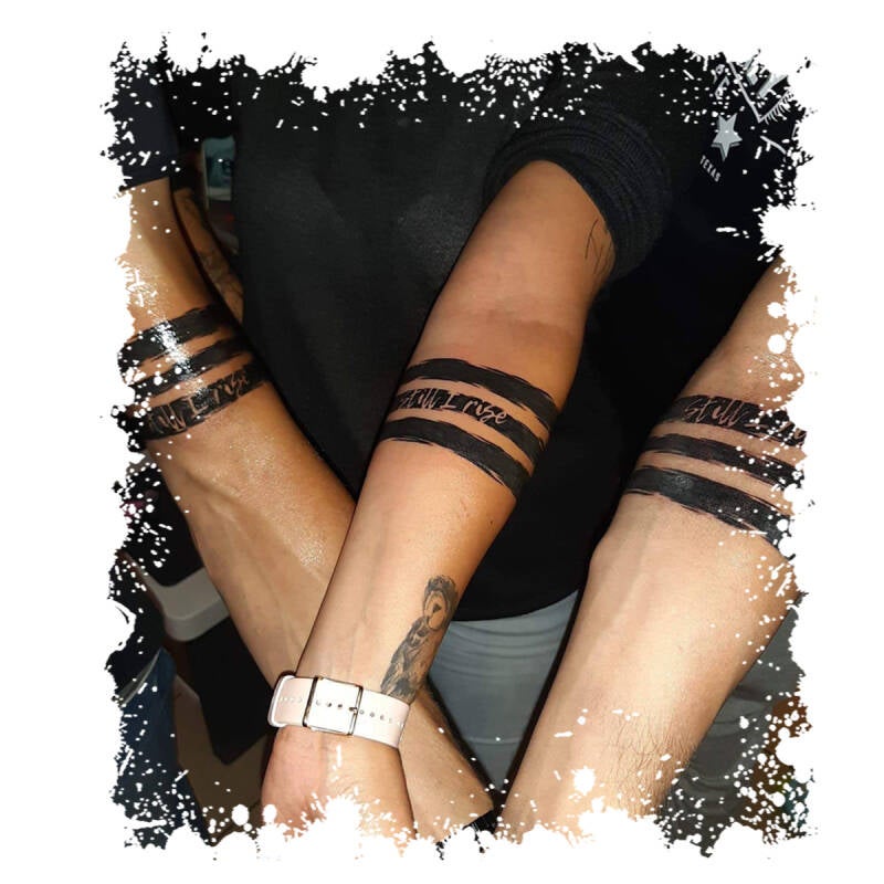 Drie onderarmen met bijpassende 'Still I Rise' tekst in zwarte banden.