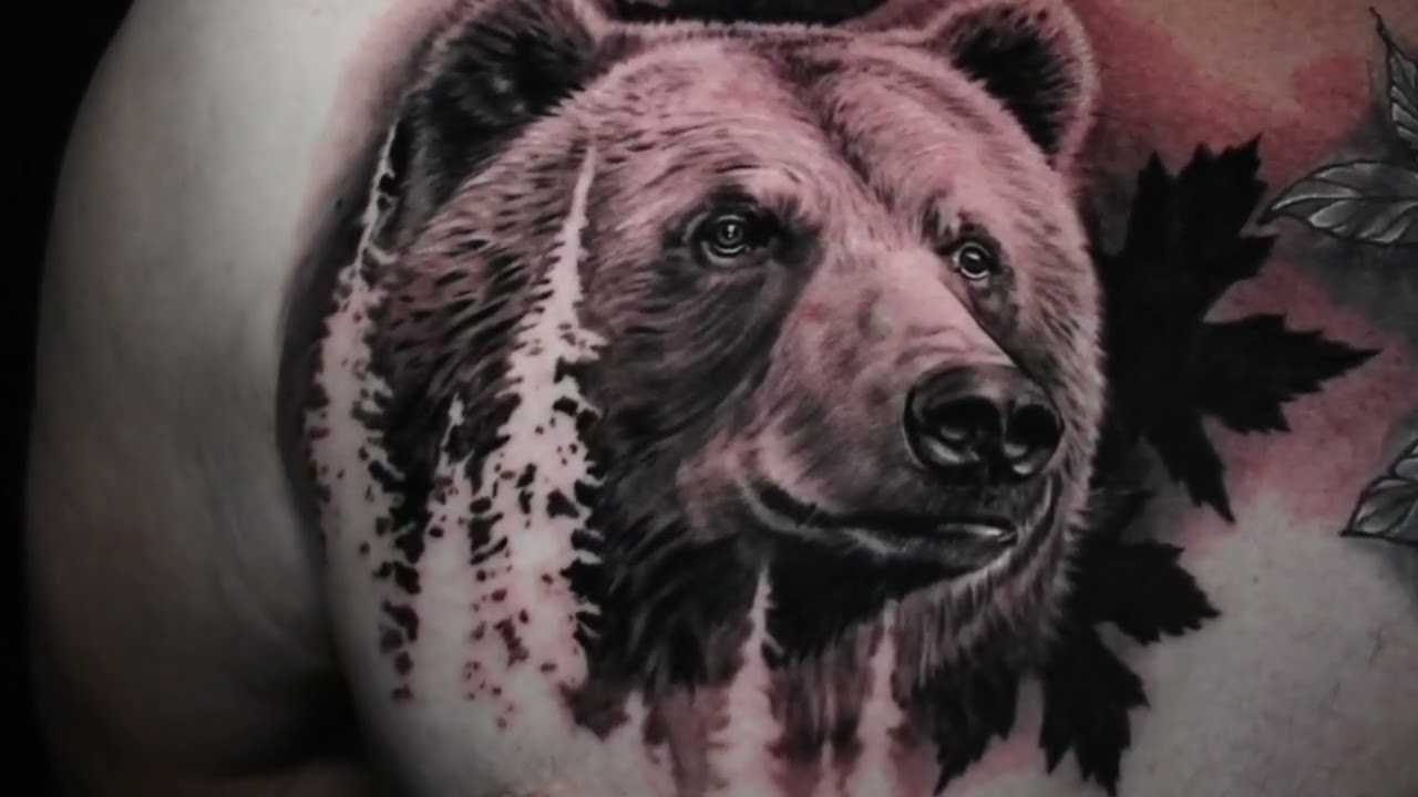 Realistische grizzlybeer tattoo met bomen en bladeren op schouder.