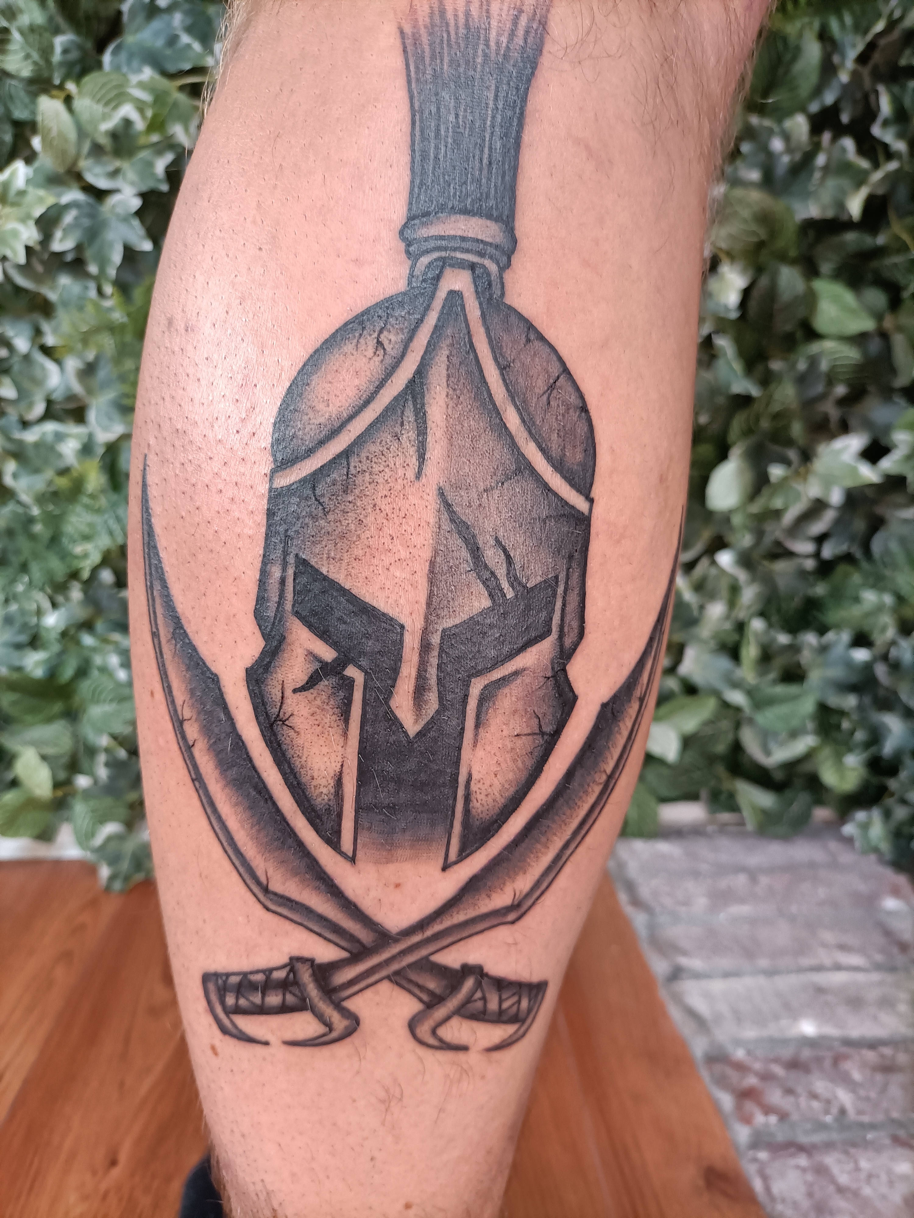 Zwart-wit Spartaanse helm met gekruiste zwaarden op onderbeen.