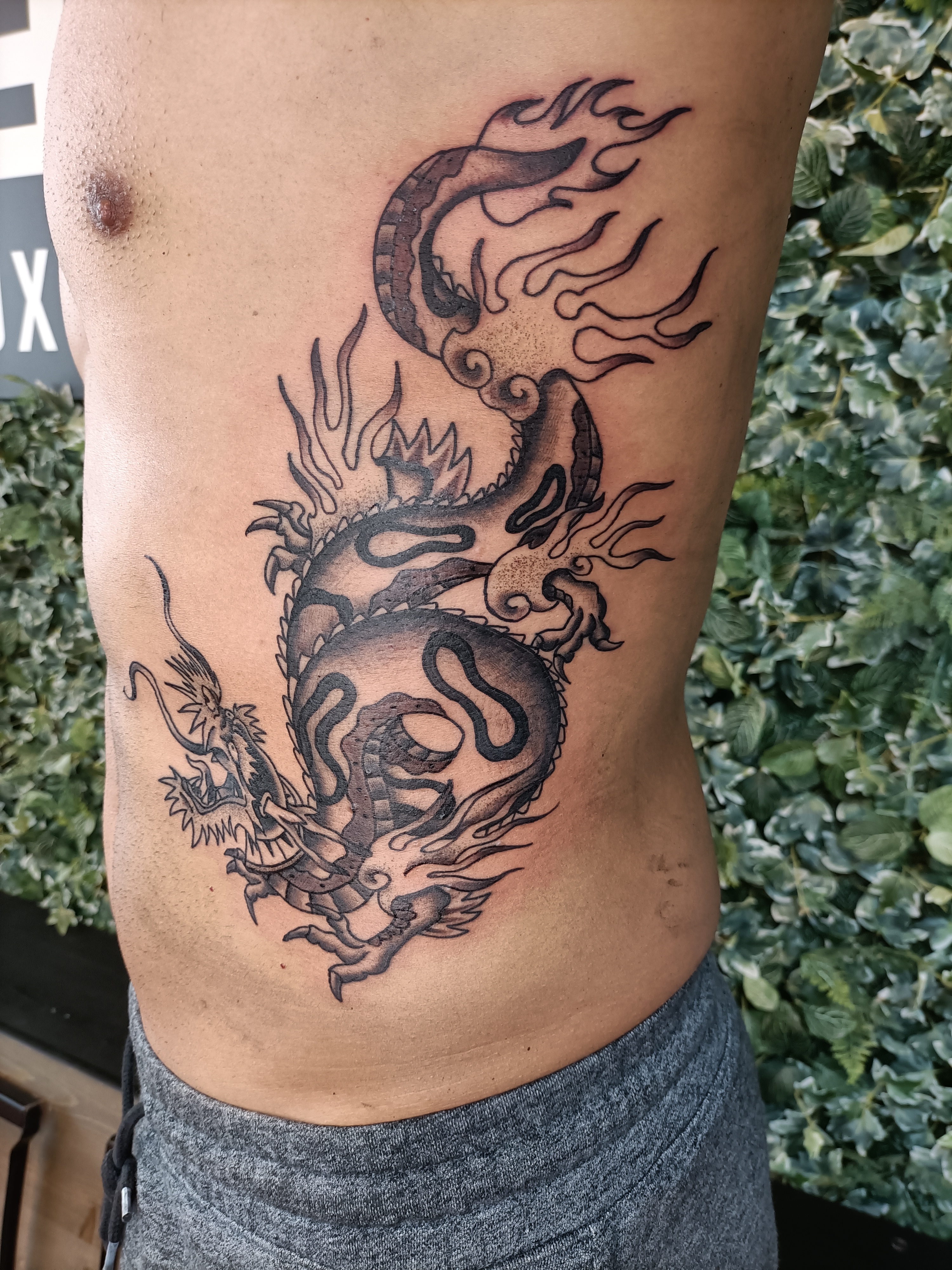 Zwart-grijze draak tattoo op de zij van het lichaam.