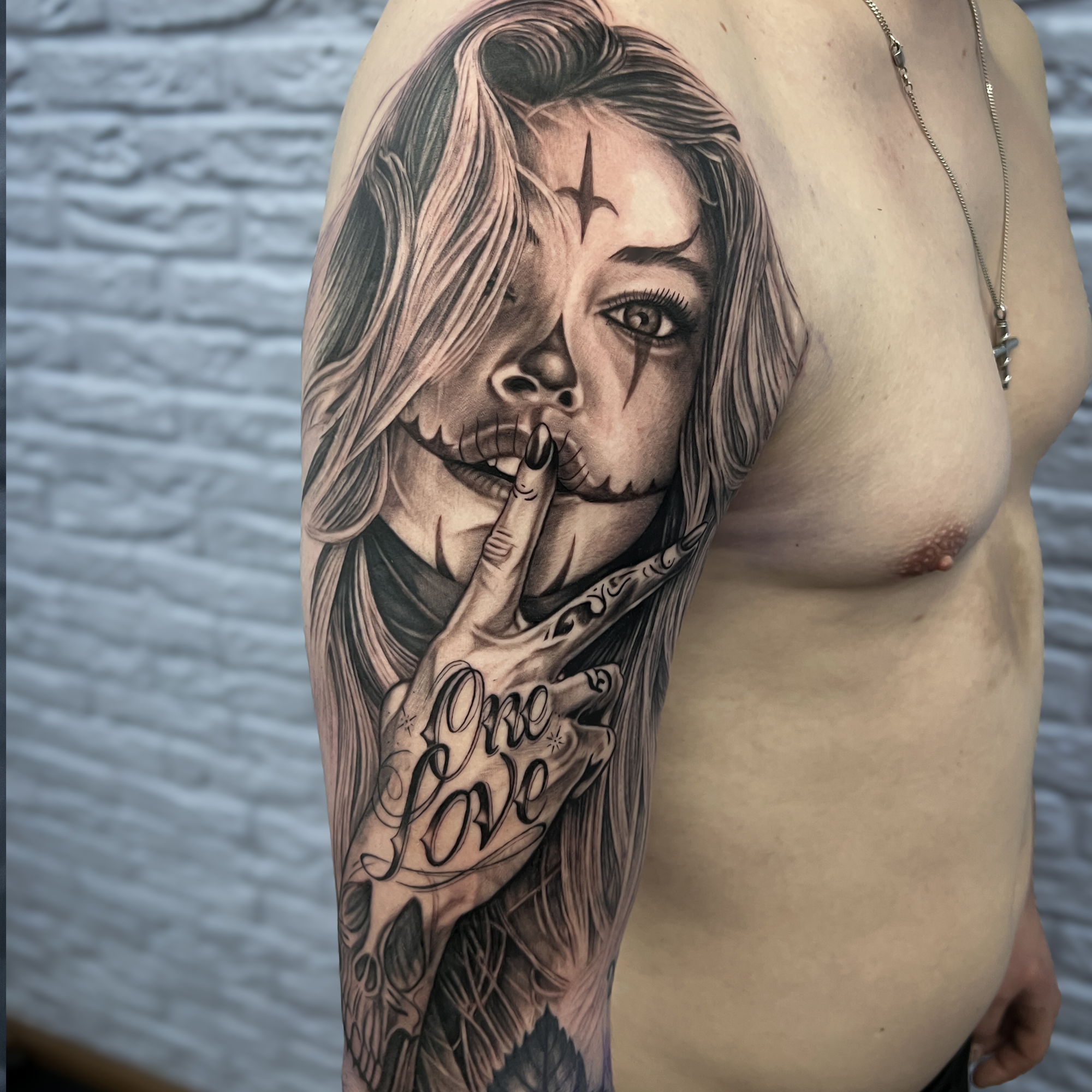 Realistisch portret van een vrouw met 'One Love' handgebaar op bovenarm.