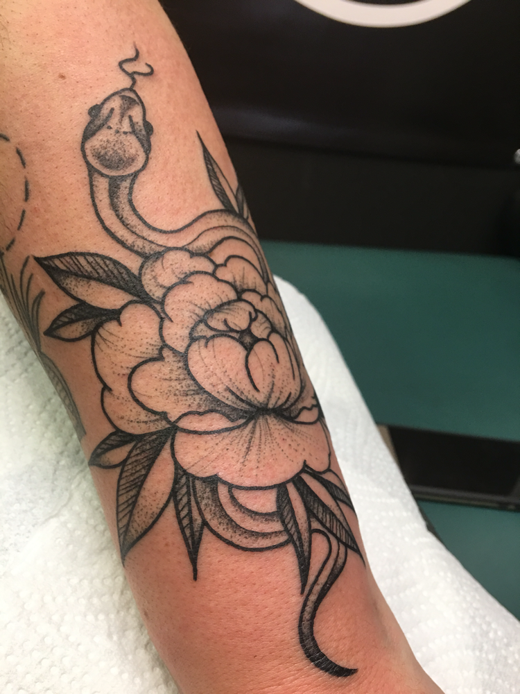 Blackwork slang en pioenroos op onderarm.