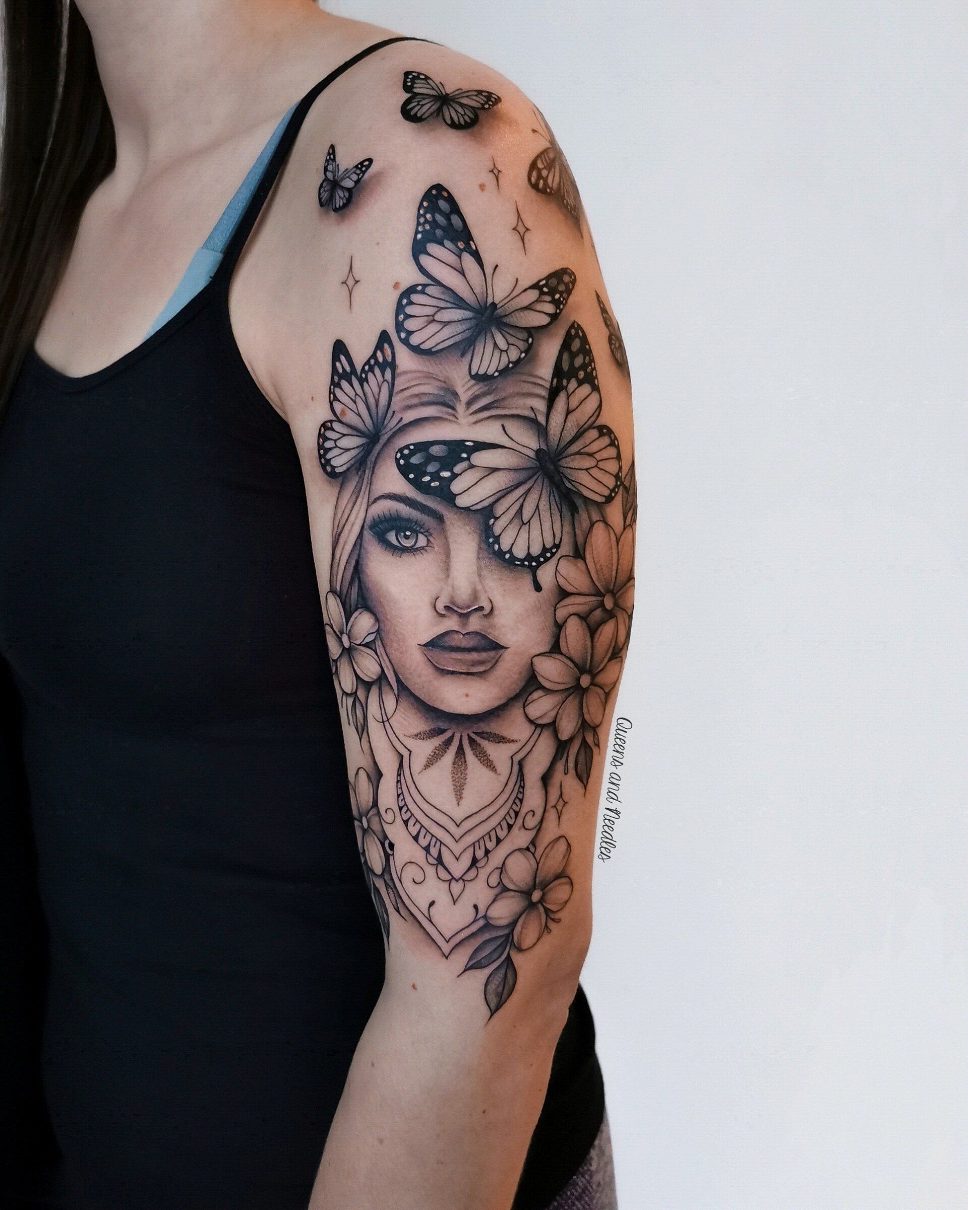 Zwart-wit portret tattoo met vlinders en bloemen op bovenarm.