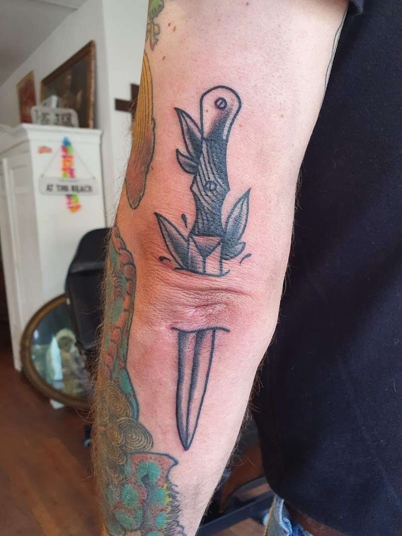 Traditionele dolk tattoo die door de huid van de elleboog steekt.