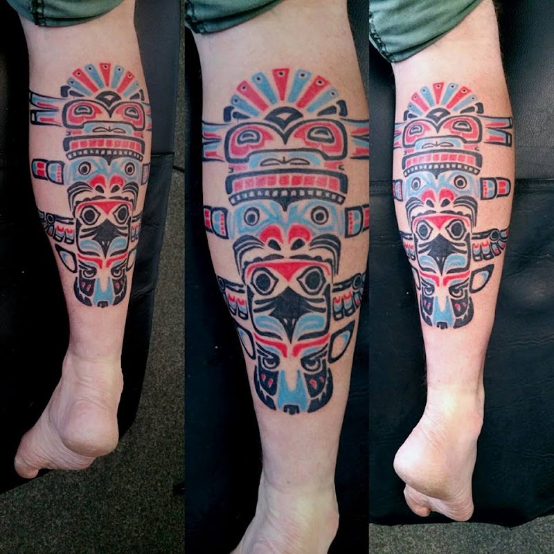 Kleurrijke totempaal tattoo op onderbeen in Haida stijl.