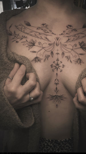 Elegante fineline ornamental tattoo op borst en buik met bloemmotieven.