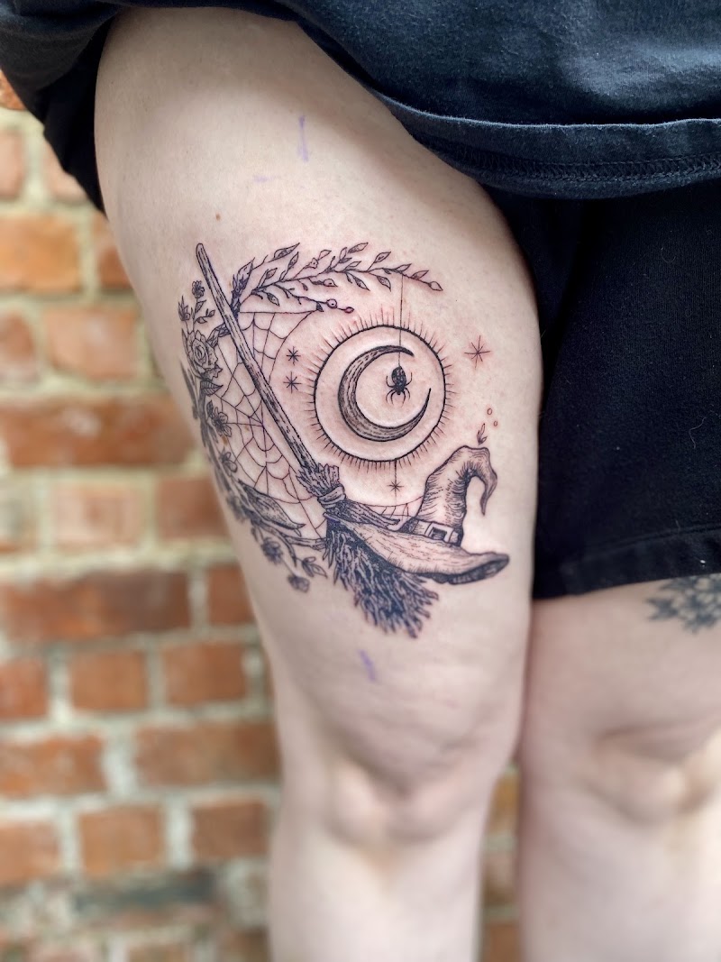 Blackwork tattoo op bovenbeen met heksenhoed, bezem, maan en spin.