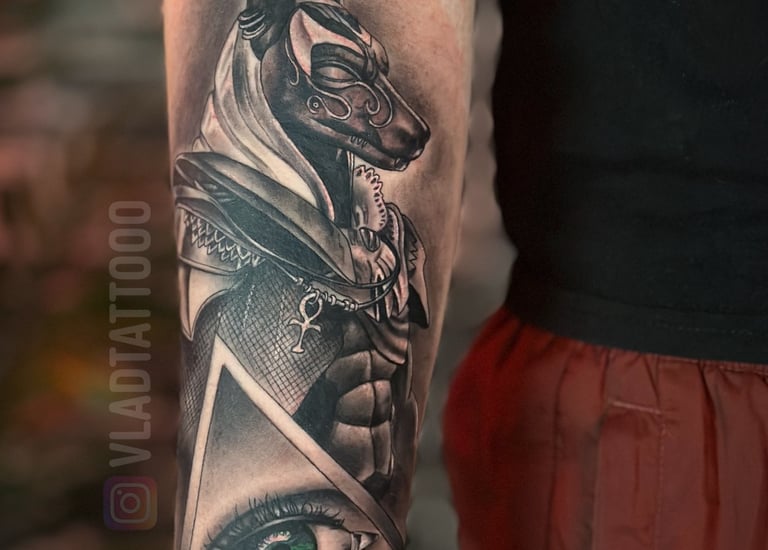 Realistische Anubis tattoo met oog in driehoek op bovenarm.
