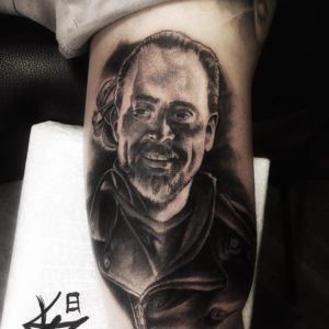 Realistisch zwart-wit portret van Negan uit The Walking Dead op de bovenarm.