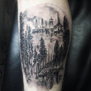 Zwart-wit tattoo van kasteel in bos met dennenappels op onderbeen.
