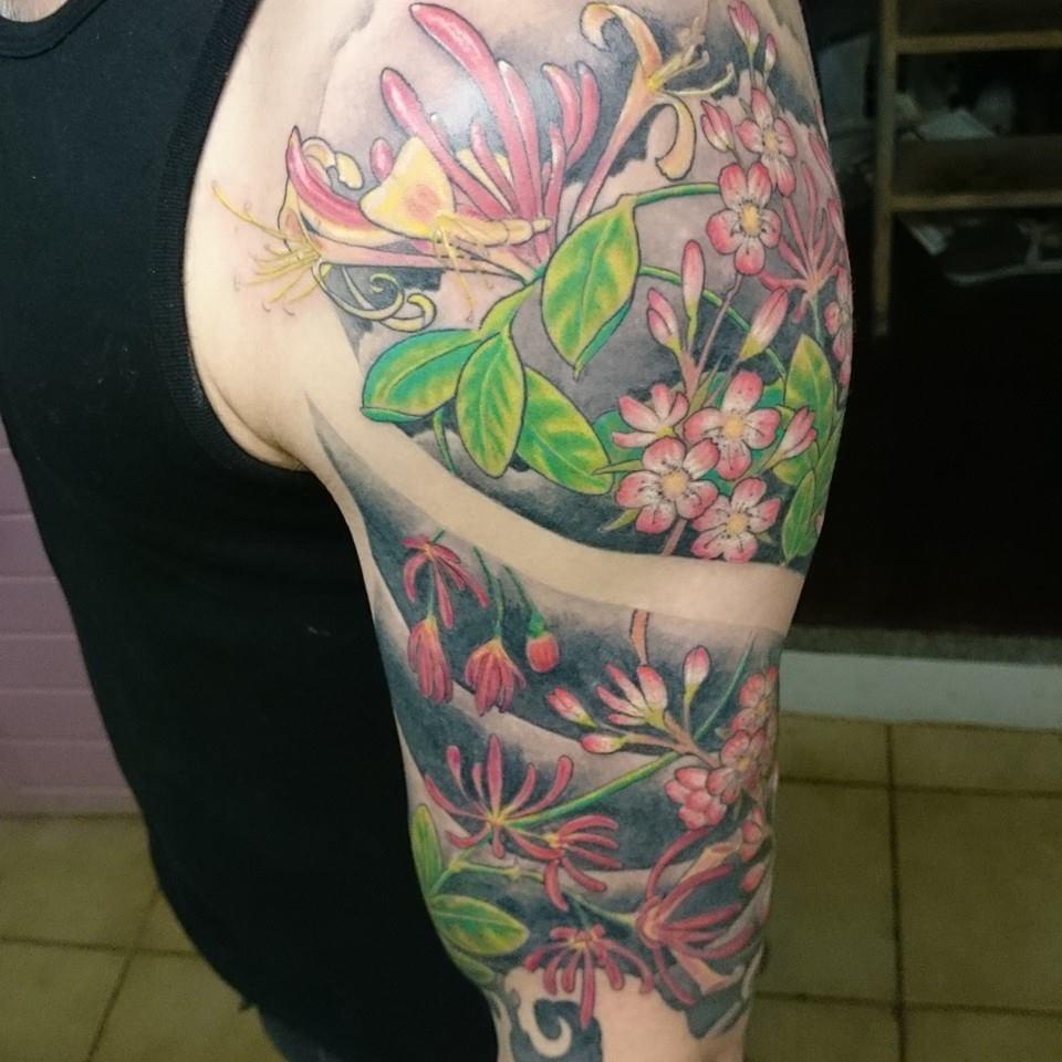 Kleurrijke half-sleeve tattoo met kamperfoelie en roze bloesem.