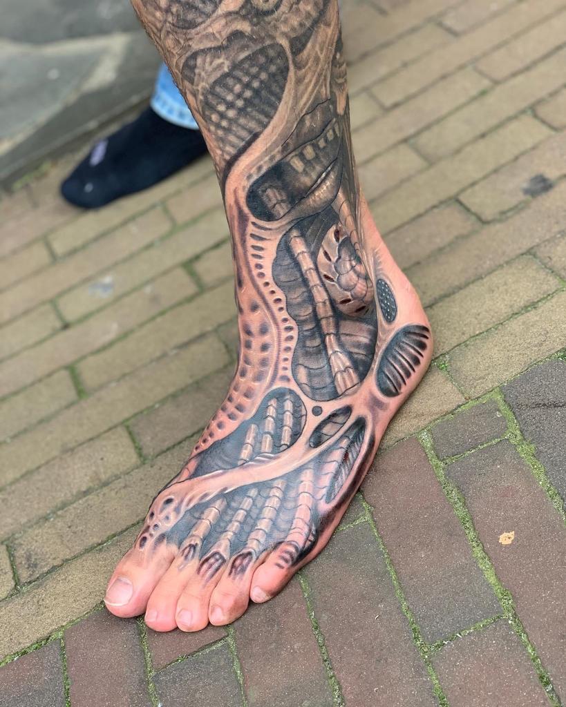 Gedetailleerde biomechanische tattoo op voet en enkel.