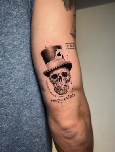 Schedel met hoge hoed, schoppenaas kaart en tekst 'impossible' op bovenarm.