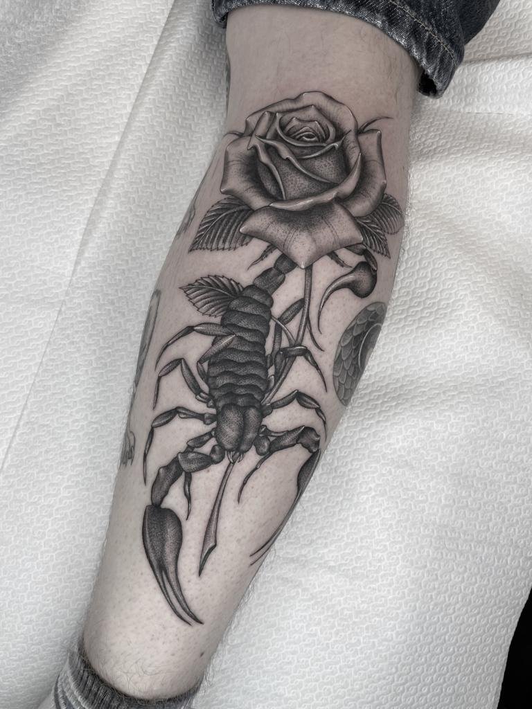 Blackwork schorpioen en roos tattoo op onderbeen.