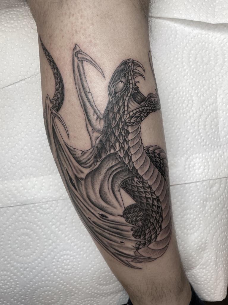 Gedetailleerde zwart-wit draak tattoo op onderbeen met schubben en vleugels.