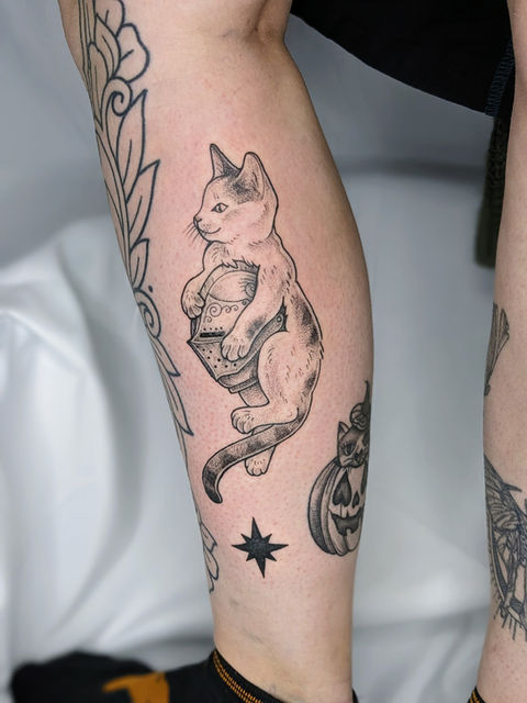 Fineline tattoo van een kat die een ridderhelm vasthoudt op het onderbeen.