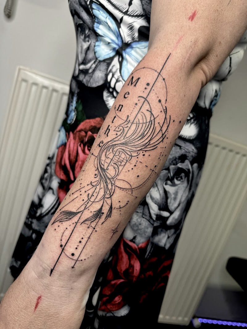 Fineline geometrische tattoo met naam 'Menthe' en veer op onderarm.