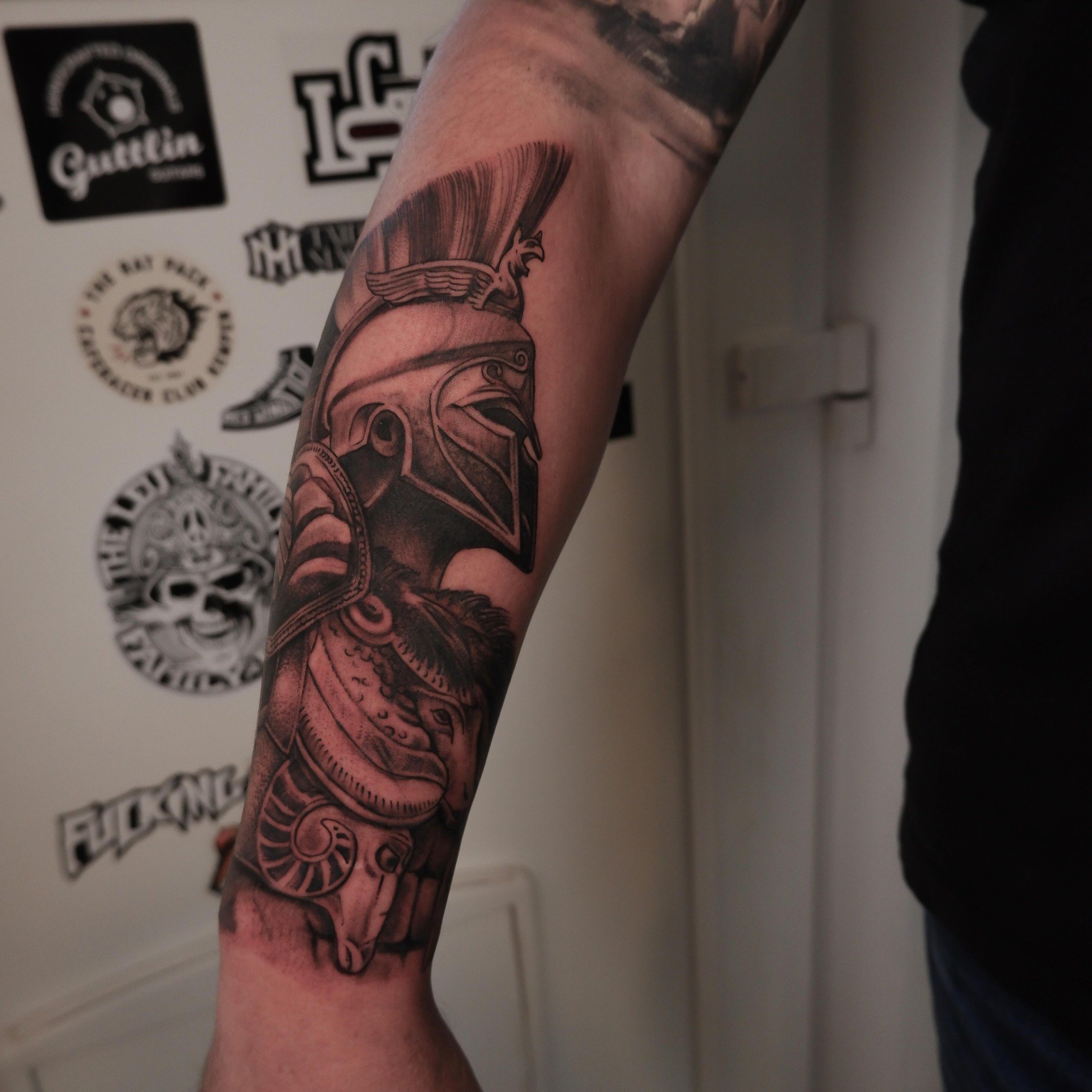 Zwart-wit tattoo van een Spartaanse krijger met helm op de onderarm.