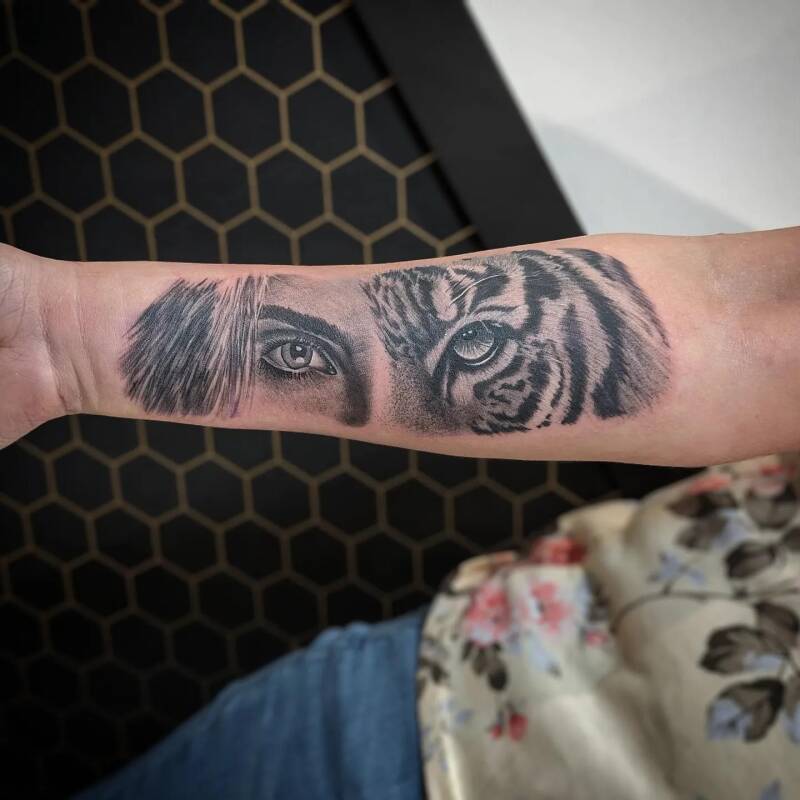 Realistische tattoo van een vrouwen- en tijgeroog op de onderarm.
