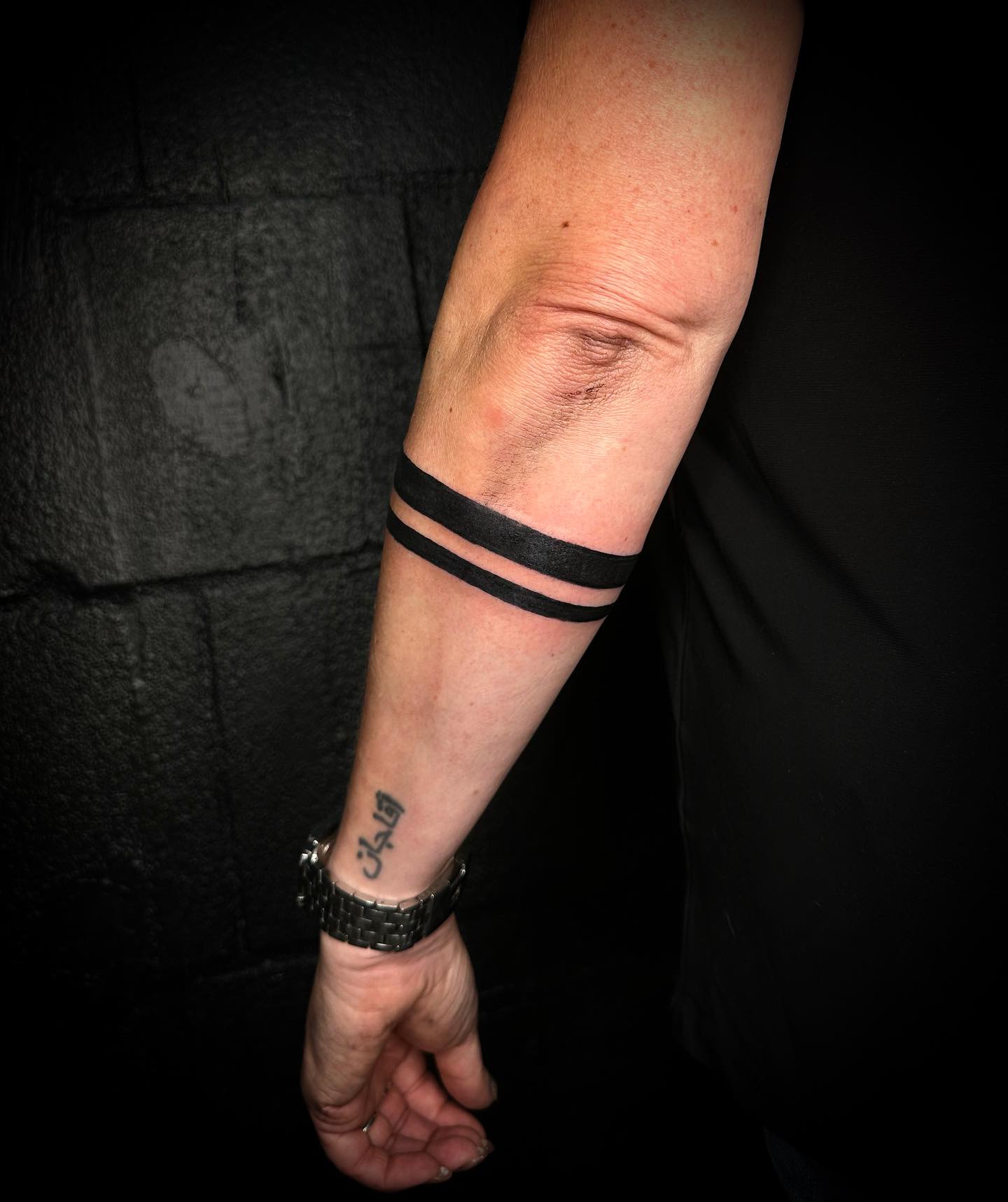 Twee massieve zwarte armbanden en Arabische tekst op de pols.