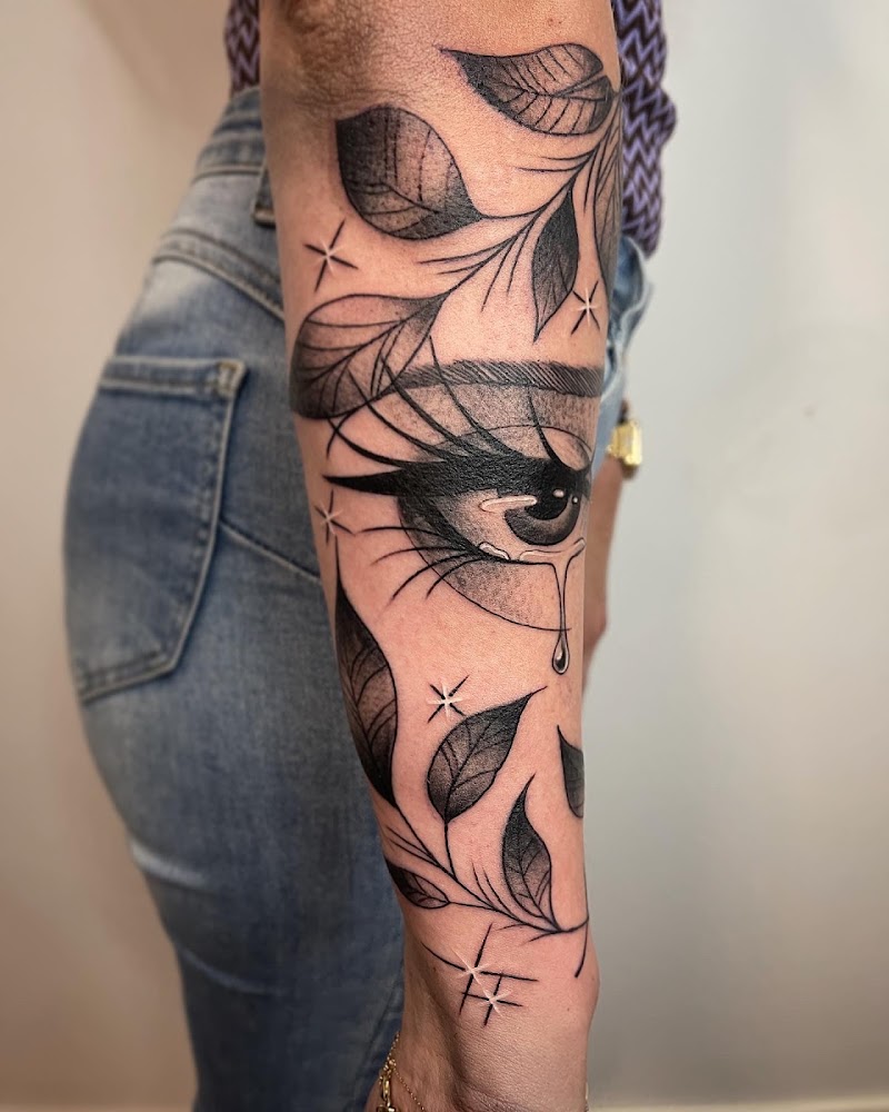 Blackwork tattoo van een huilend oog met bladeren en sterren op de onderarm.