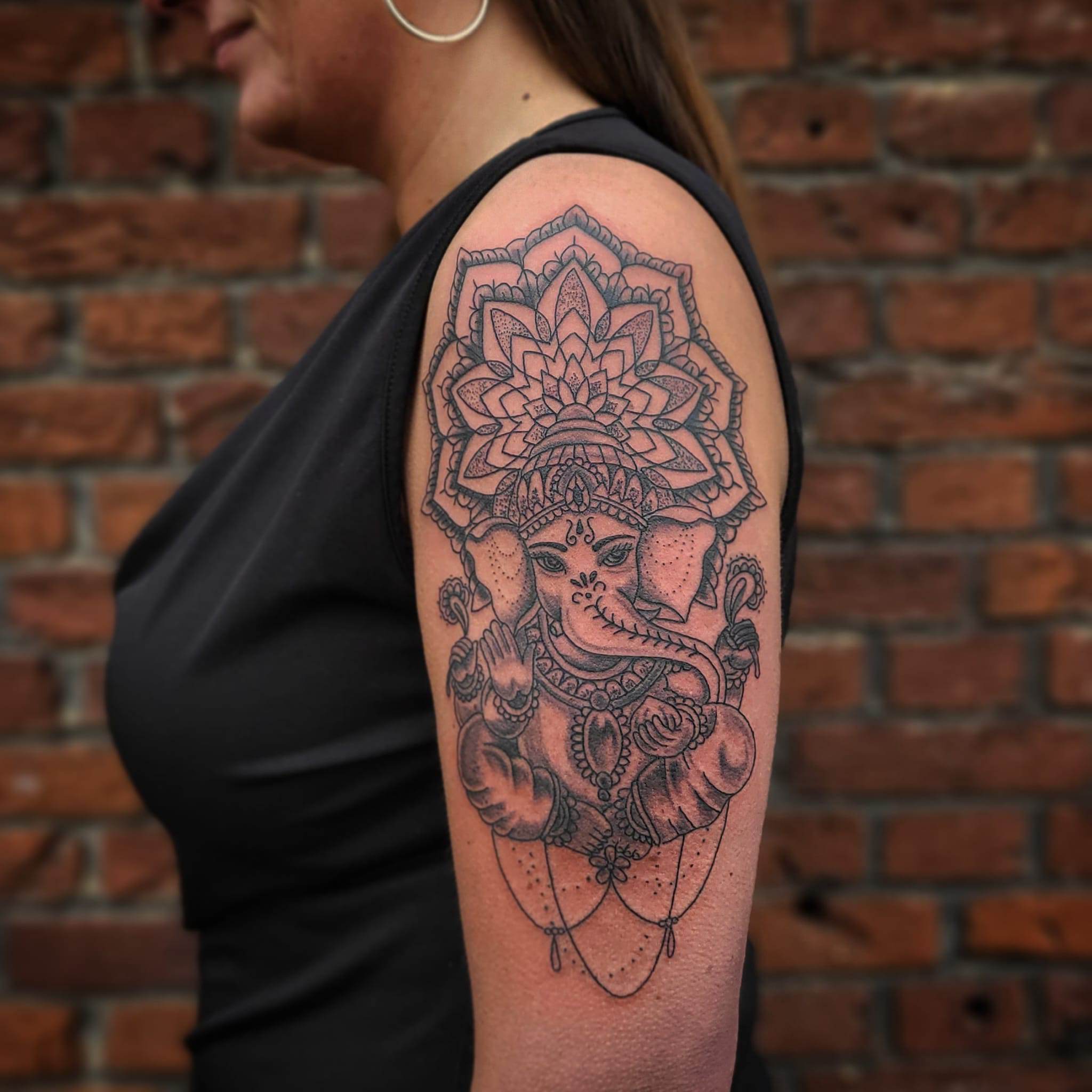 Gedetailleerde Ganesha tattoo met mandala op bovenarm.
