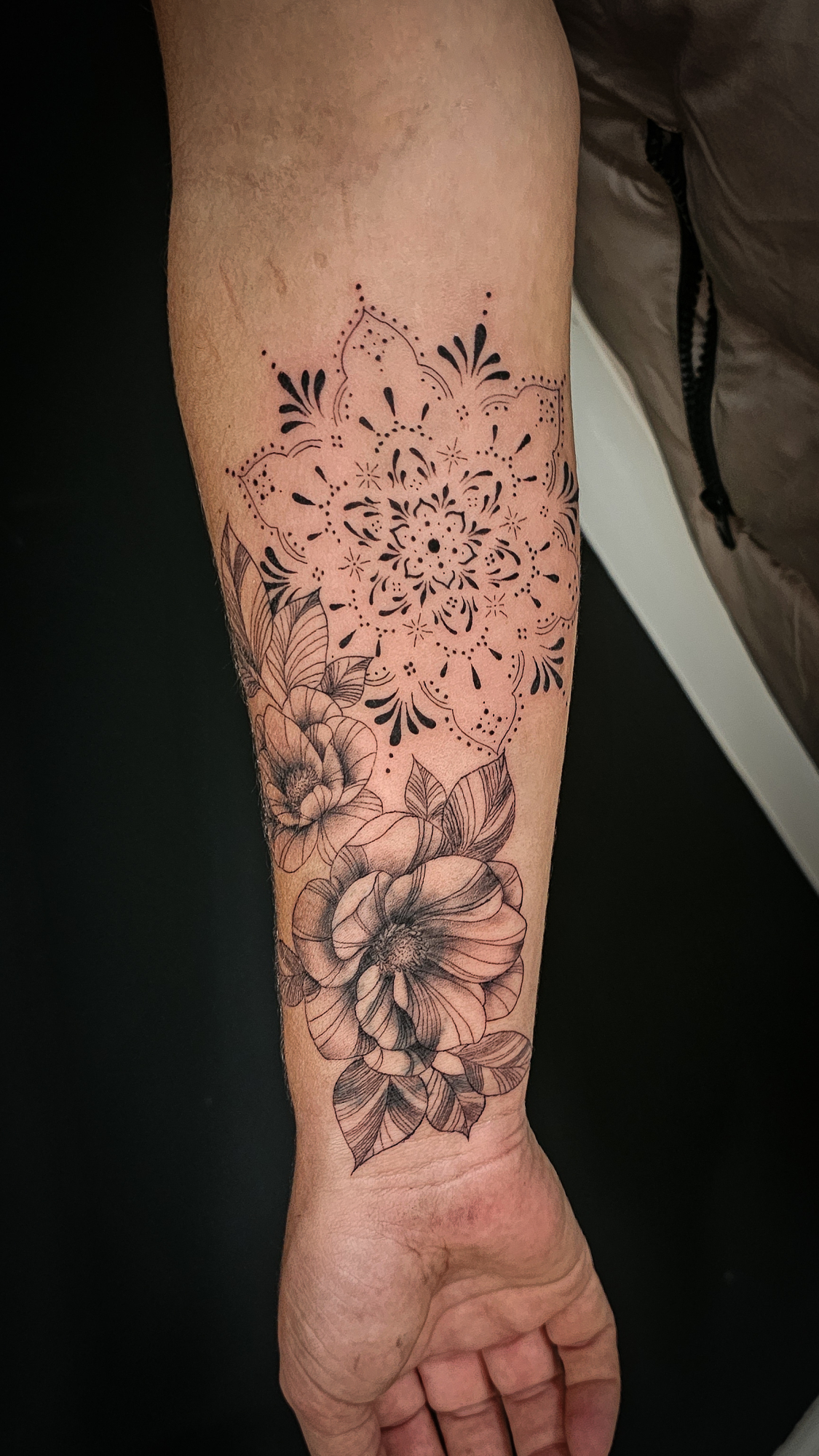Fineline en dotwork mandala met bloemen op de onderarm.