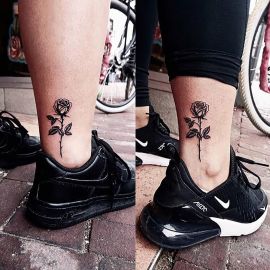 Minimalistische zwarte roos tattoo op de enkel.