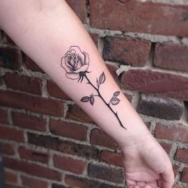 Zwart-wit fineline roos met steel en bladeren op onderarm.