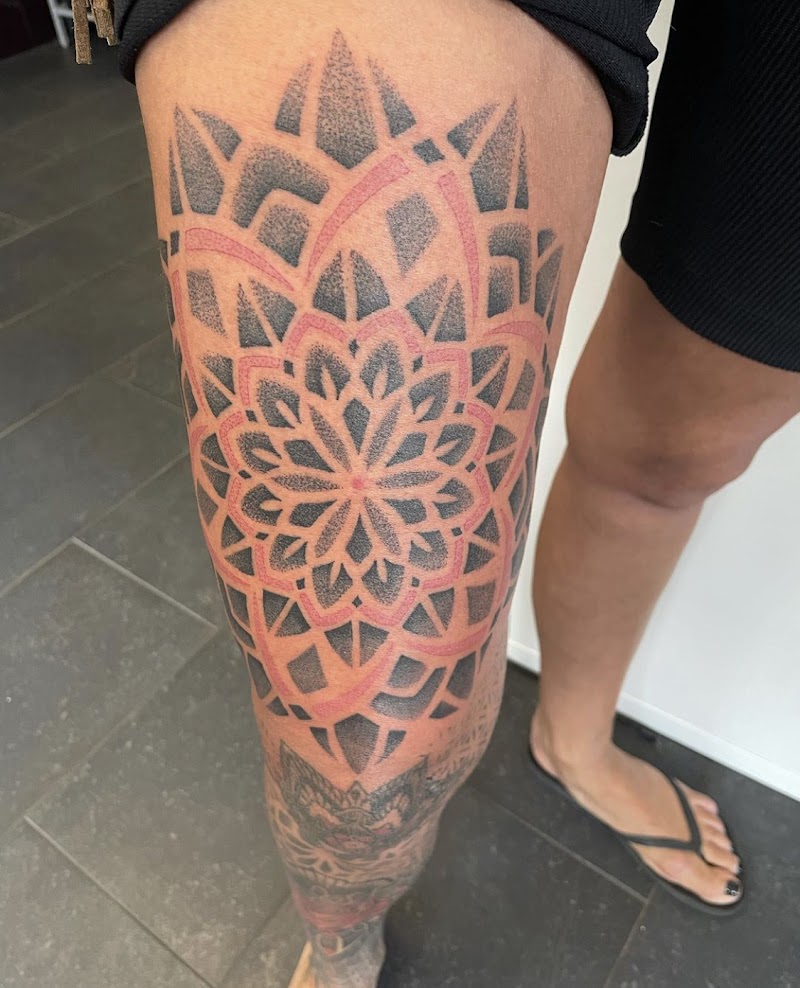 Grote geometrische mandala tattoo op bovenbeen met rood en zwart dotwork.