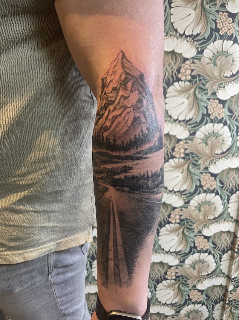 Zwart-wit landschap tattoo met berg, bos en weg op onderarm.