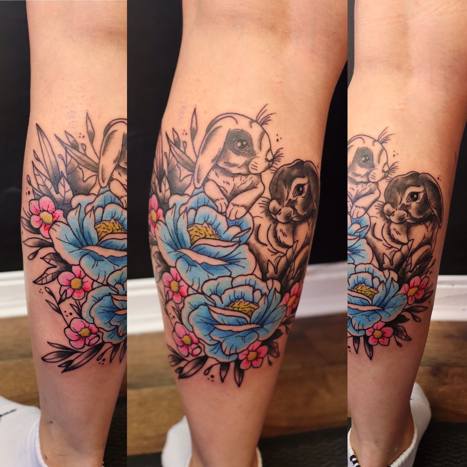 Neo-traditionele tattoo van twee konijnen met blauwe en roze bloemen op onderbeen.