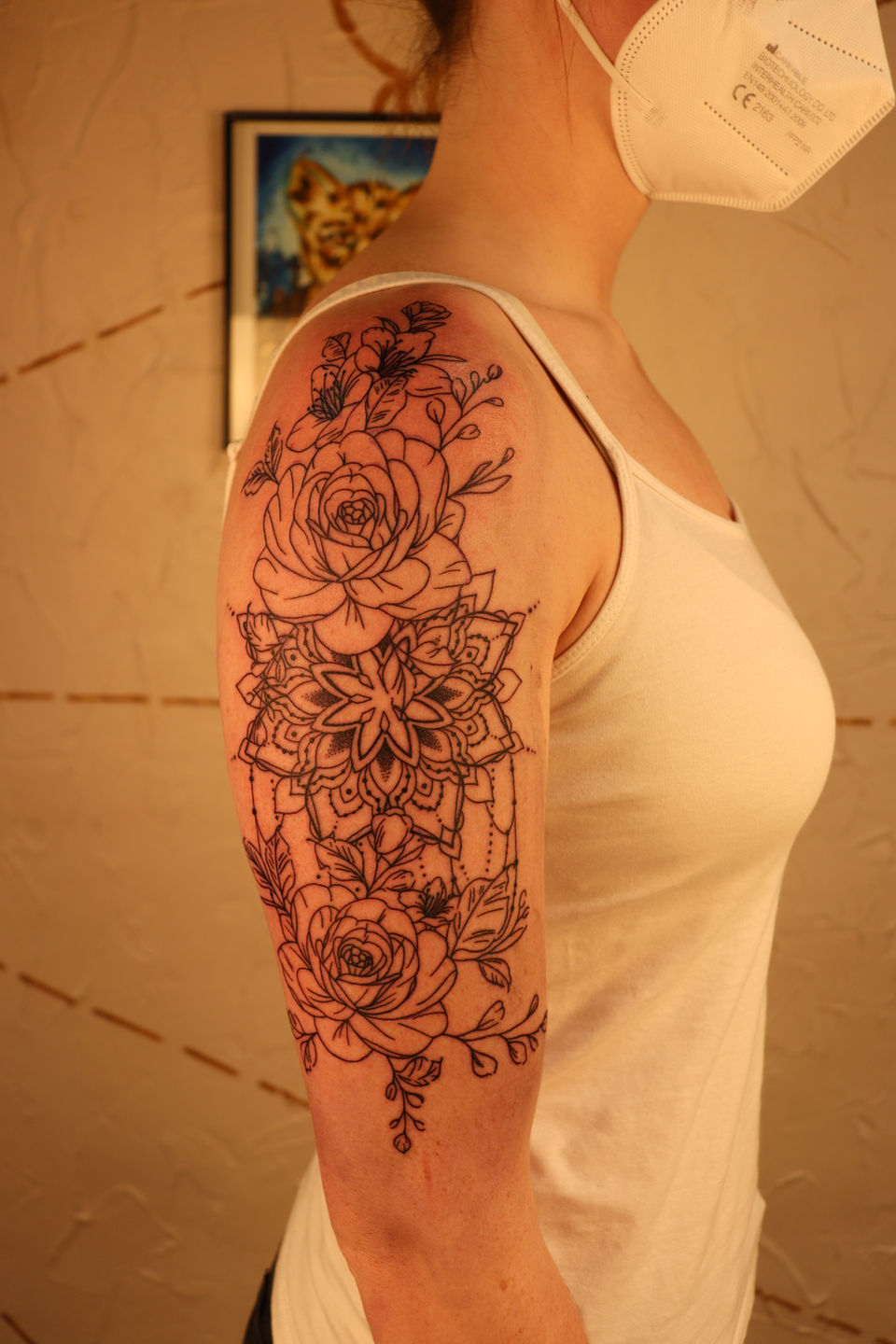 Fineline bloemen en mandala tattoo op bovenarm.