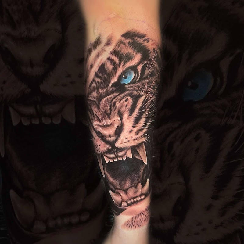 Realistische tijgerkop met blauwe ogen en open bek op onderbeen.