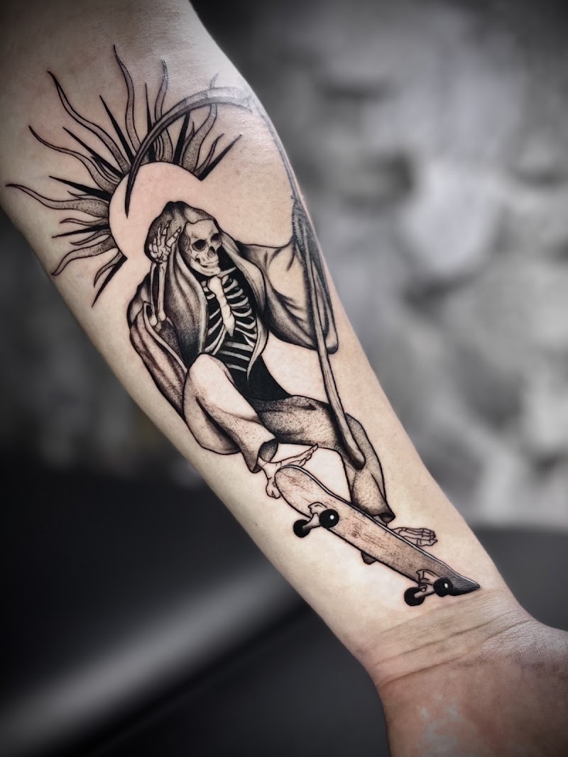 Zwart-wit tattoo van een skatende Magere Hein met zeis en stralenkrans.