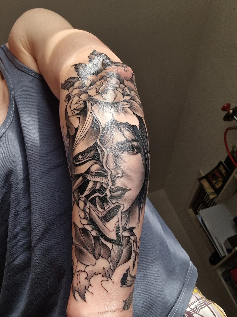 Zwart-wit tattoo van een vrouwengezicht dat overgaat in een Hannya masker met bloemen.