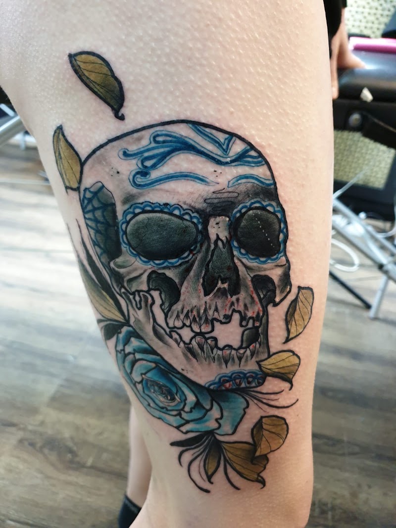 Schedel met blauwe roos en bladeren op bovenbeen.