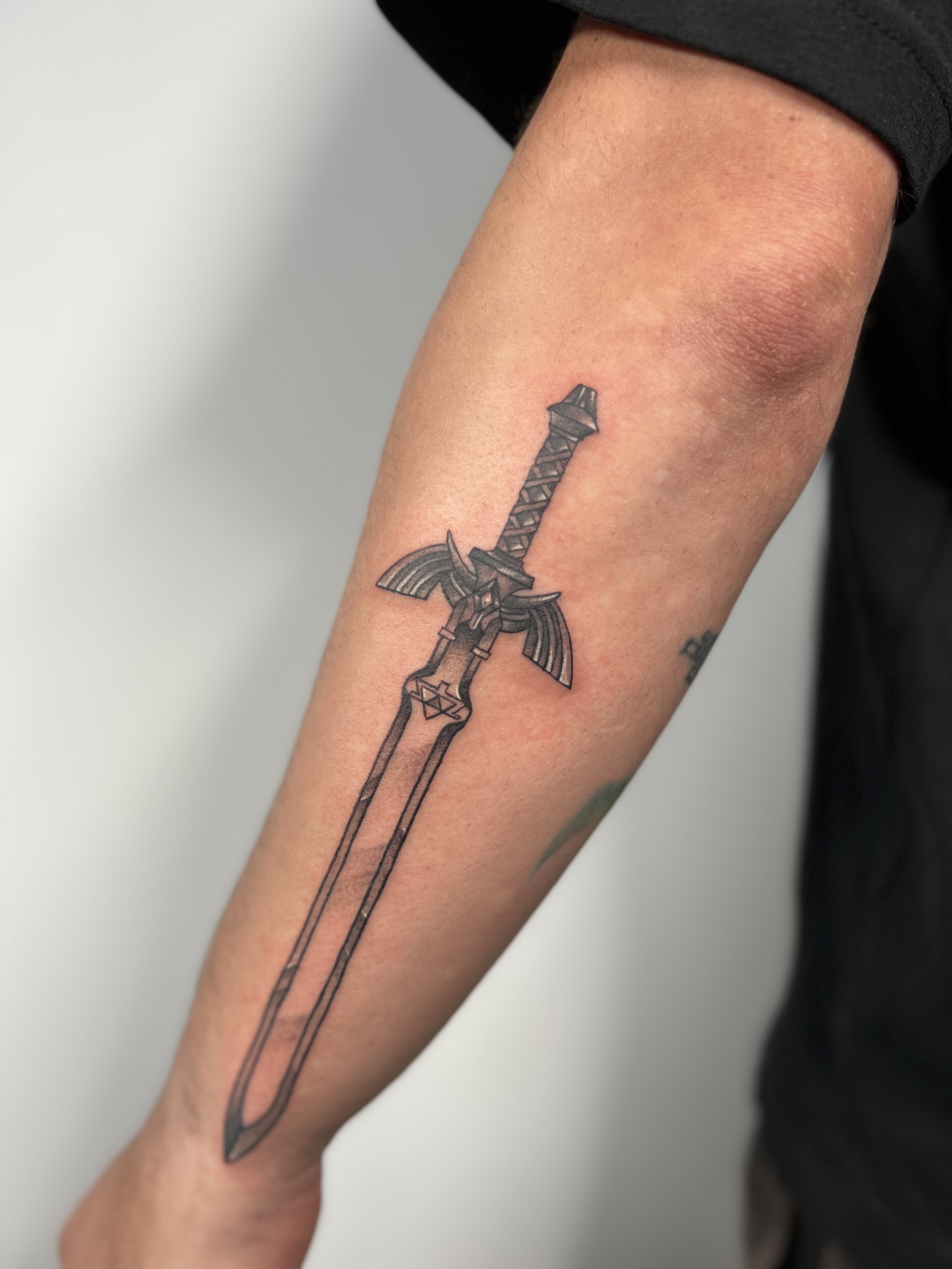 Fineline tattoo van het Master Sword uit Zelda op de onderarm.