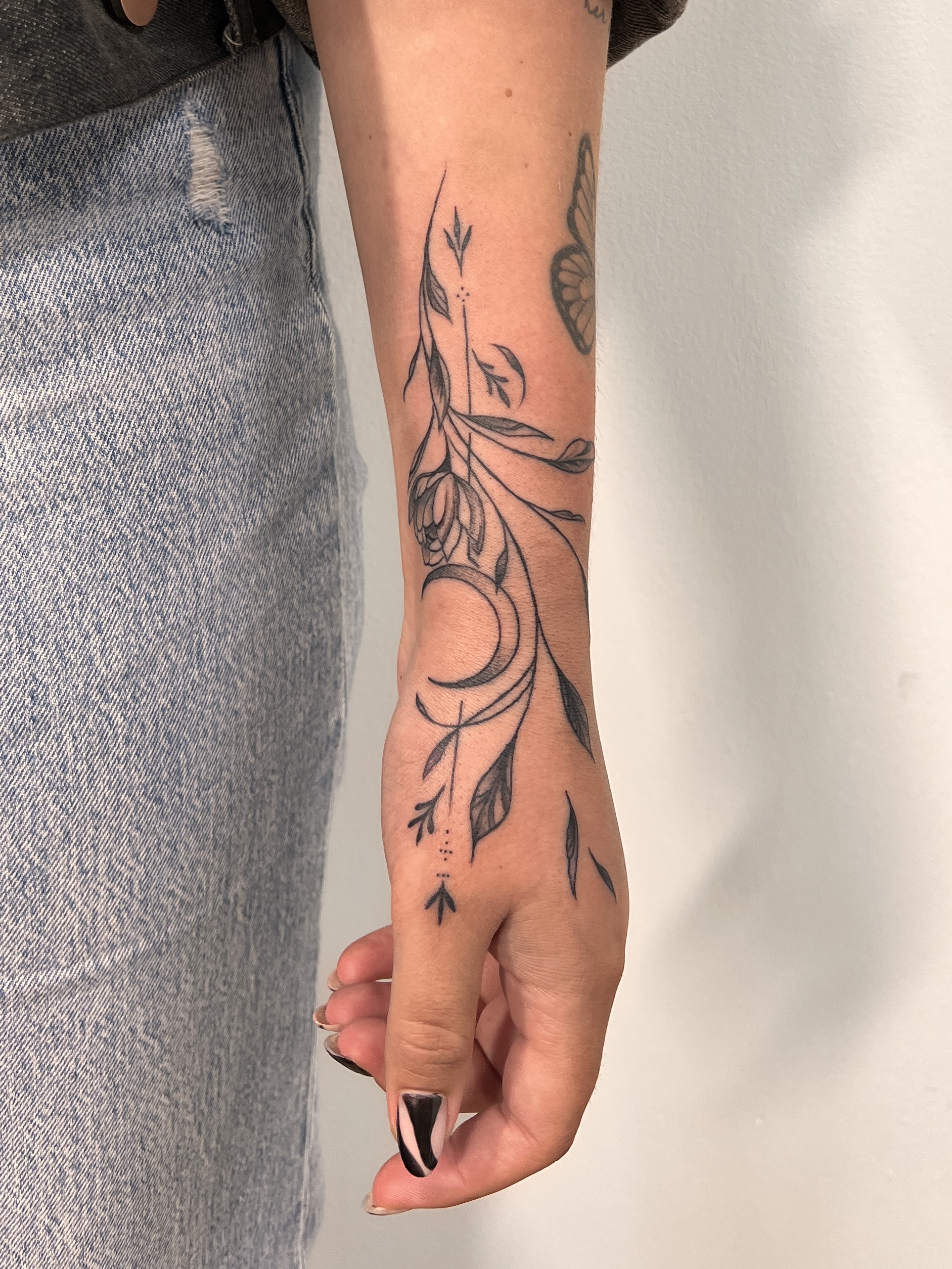 Fineline bloemen en maan tattoo op hand en pols.