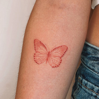Rode fineline vlinder tattoo op de bovenarm.