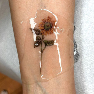 Realistische zonnebloem tattoo op de onderarm, bedekt met folie.