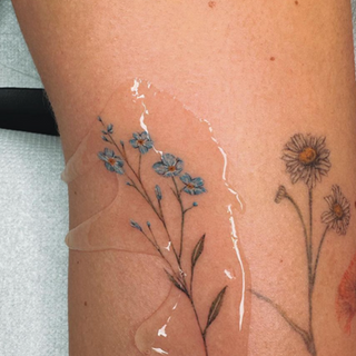 Fijne lijn bloementattoos: blauwe vergeet-mij-nietjes en madeliefjes.