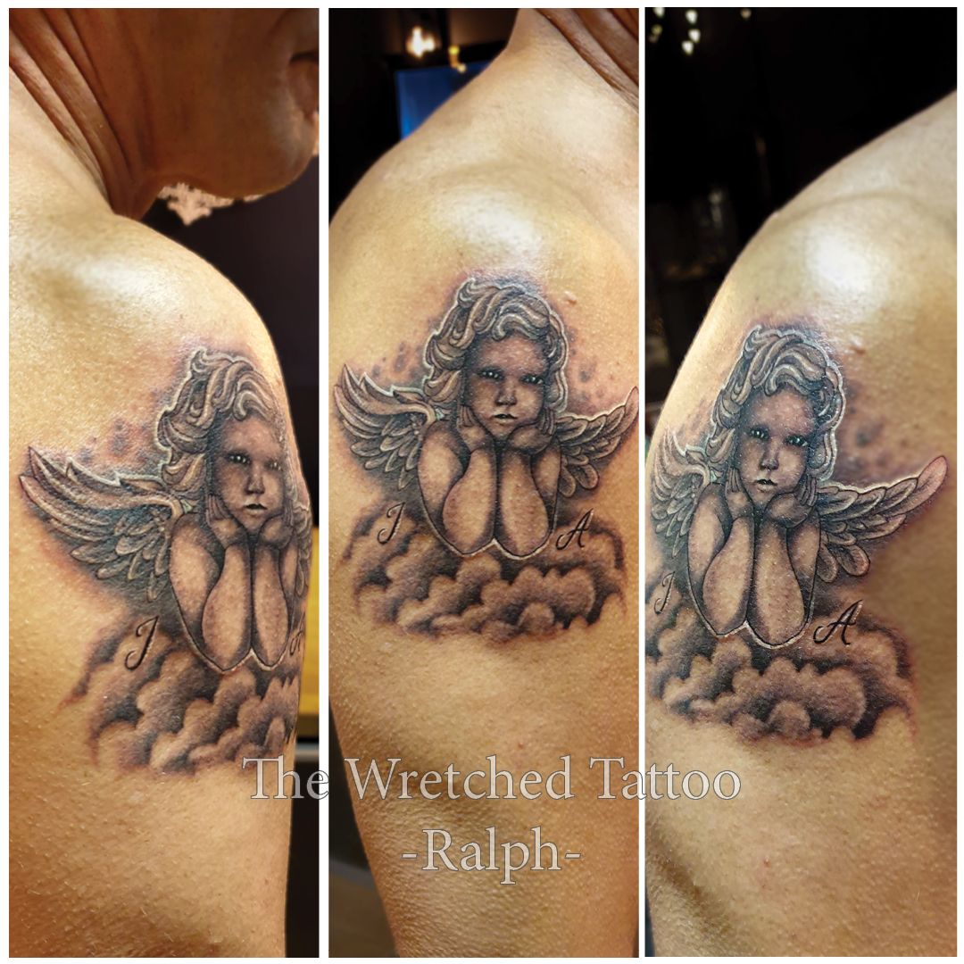 Zwart-wit cherubijntje op wolken met initialen J en A op de bovenarm.