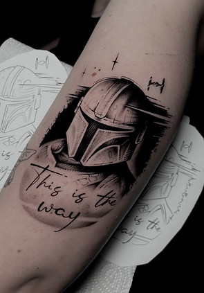 Zwart-wit Mandalorian helm tattoo met tekst "This is the way" op onderarm.
